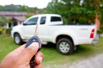 A hand holding a key fob in front of a white pickup truck mobile view