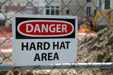 A sign on a fence of a construction site that says DANGER HARD HAT AREA mobile view