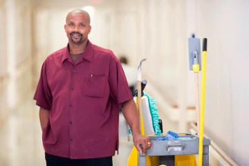 Janitor smiling next to a cart full of cleaning equipment mobile view