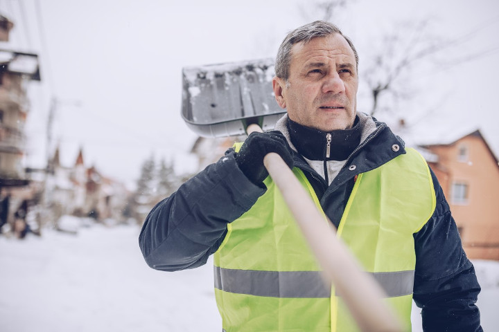 Man holding a snow shovel over his shoulder mobile view