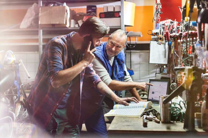 2 men leaning over a work bench discussing materials while one is on the phone