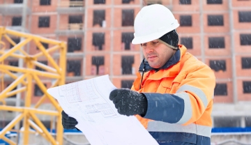 Construction worker dressed in winter clothes looking over plans