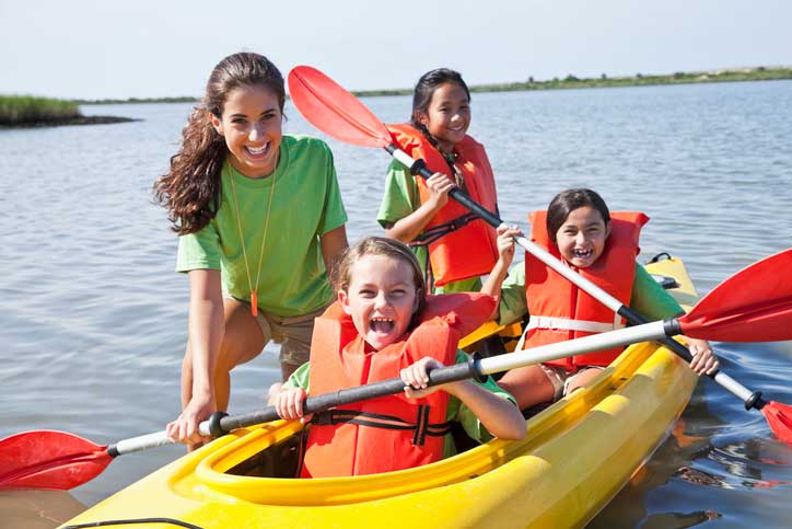A camp counselor and three campers in a kayak on the water.