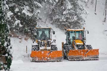 Two yellow commercial snow plows parked in a snowy parking lot