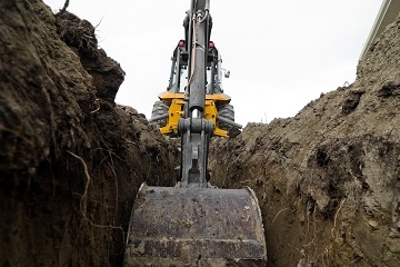 A backhoe digs a hole in dark soil