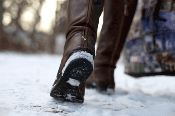 Close up of someone's boots as they walk on an icy sidewalk mobile view
