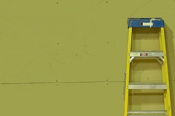 A yellow aluminum step ladder leans against drywall on a construction site